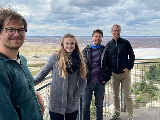 Four people stand on a viewing platform at the Nochten opencast mine and smile at the camera.