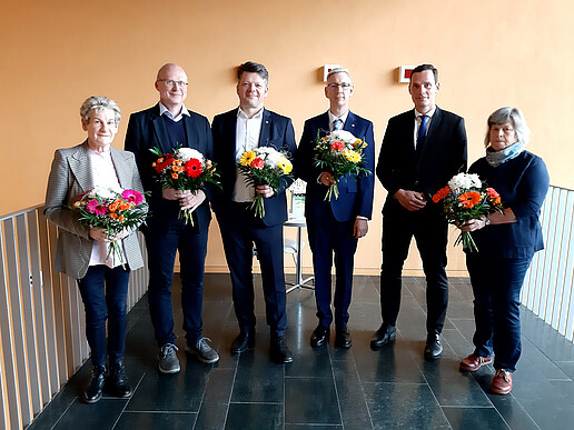 Sechs Personen des Hochschulrates stehen im Flur, halten Blumensträuße und lächeln in die Kamera.