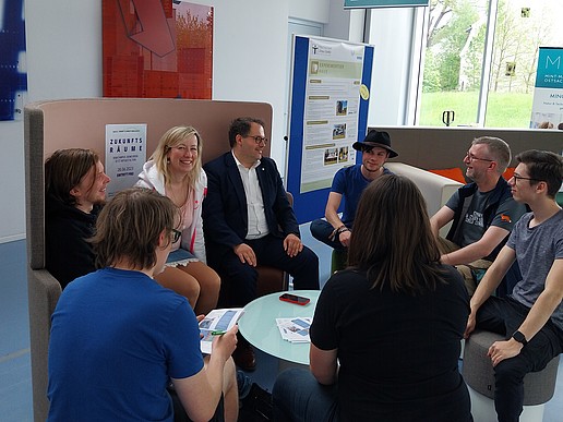 Rector and Vice-Rector sit with students in the furniture exhibition.